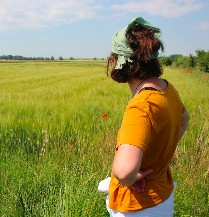 Une femme se tient devant un champ de blé et le regarde, dos à l'objectif